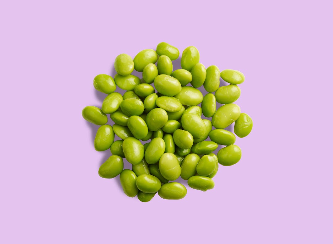 A vibrant pile of fresh green edamame beans rests on a soft purple background.