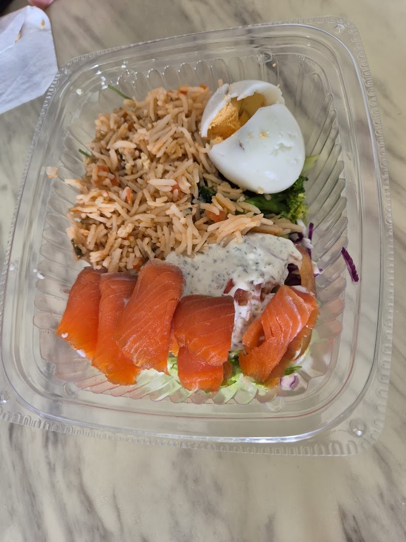 A clear plastic container holds a healthy meal with rice, smoked salmon, a hard-boiled egg, and fresh salad.