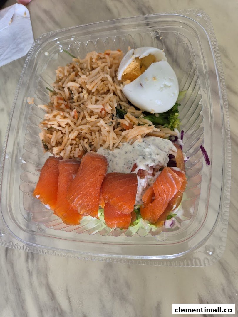 A clear plastic container holds a healthy meal with rice, smoked salmon, a hard-boiled egg, and fresh salad.