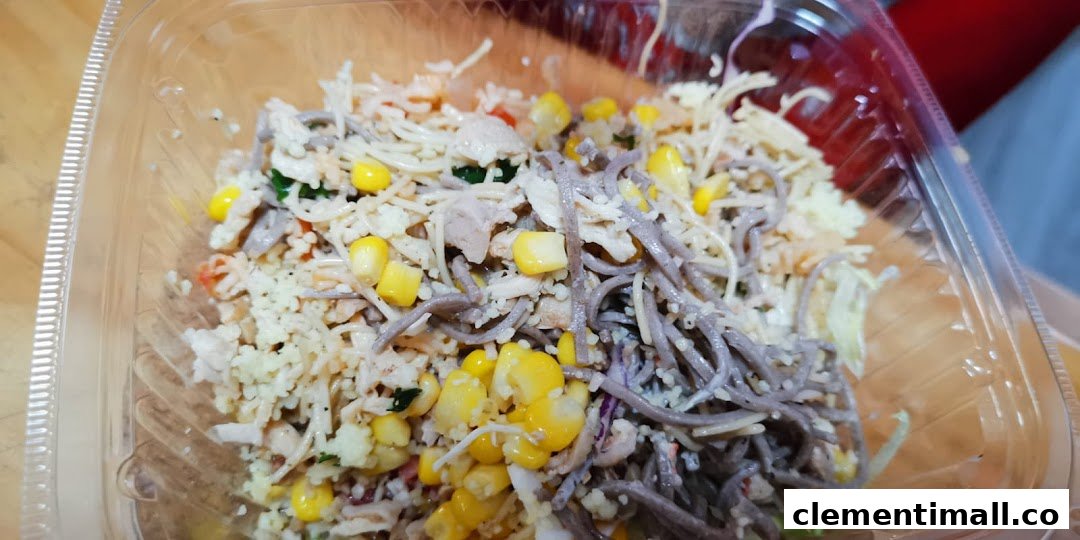 A close-up of a vibrant, customizable food bowl featuring noodles, corn, and protein in a clear container.