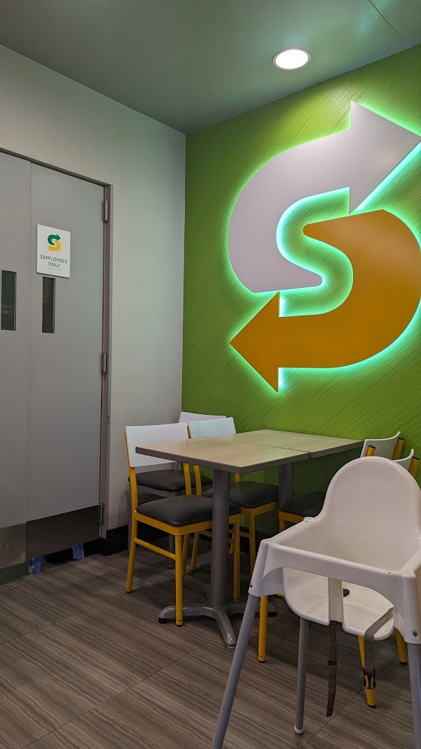 Interior view of Subway dining area with tables, chairs, and a large illuminated logo.