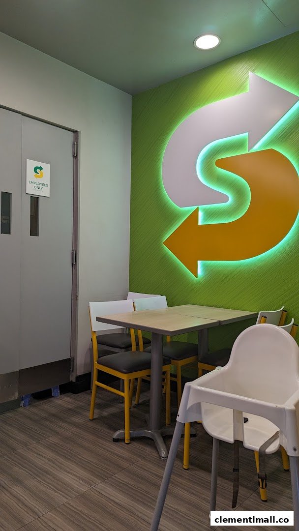 Interior view of Subway dining area with tables, chairs, and a large illuminated logo.