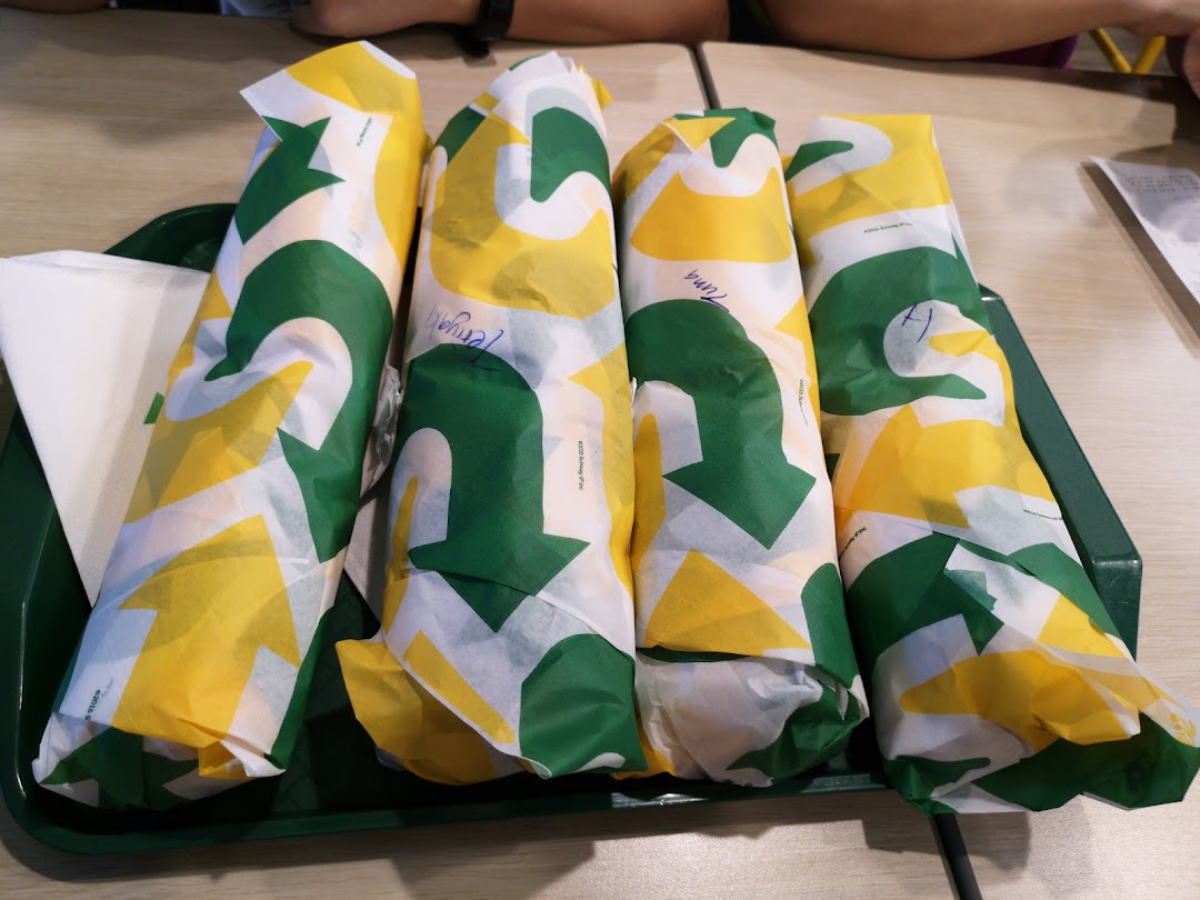 Four freshly wrapped Subway sandwiches are neatly arranged on a green serving tray.