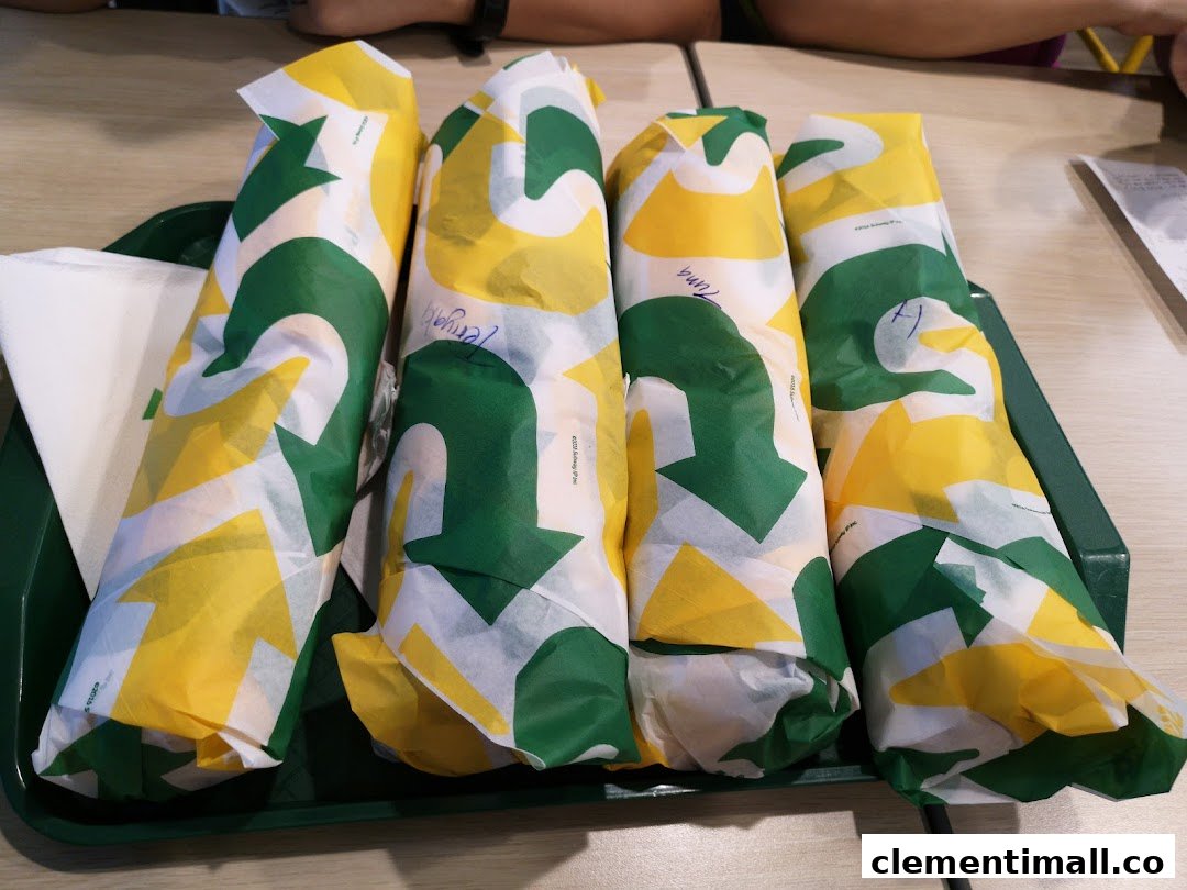 Four freshly wrapped Subway sandwiches are neatly arranged on a green serving tray.
