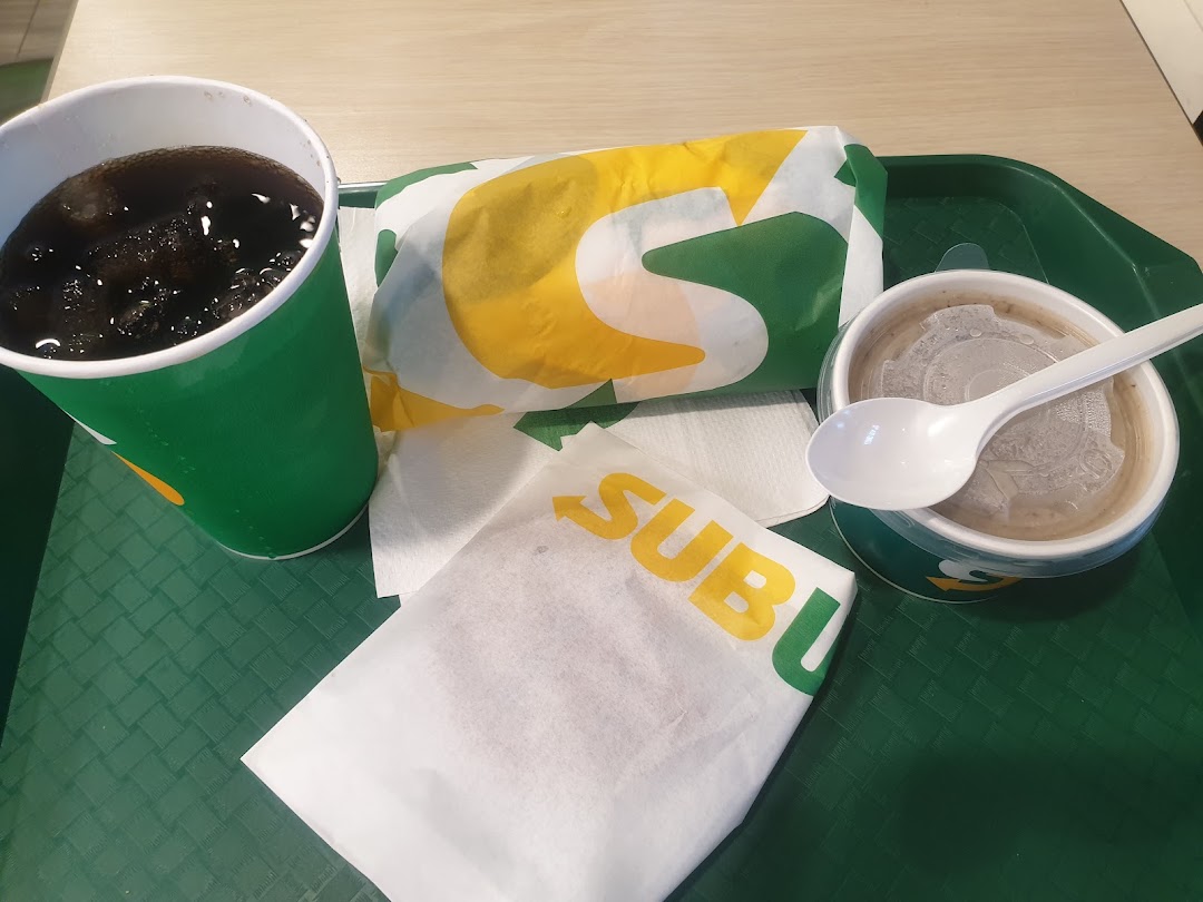 A Subway meal featuring a wrapped sandwich, a drink, and a side dish on a green tray.