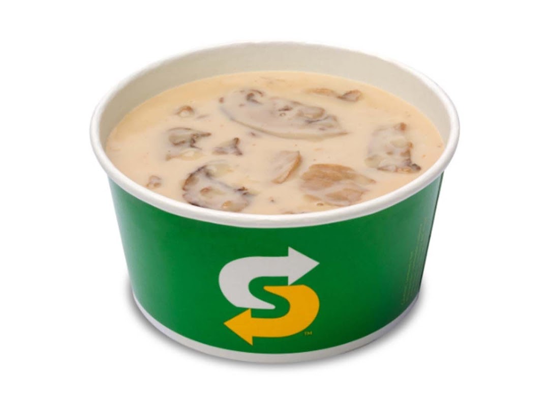 A close-up of a creamy mushroom soup in a green Subway branded cup.