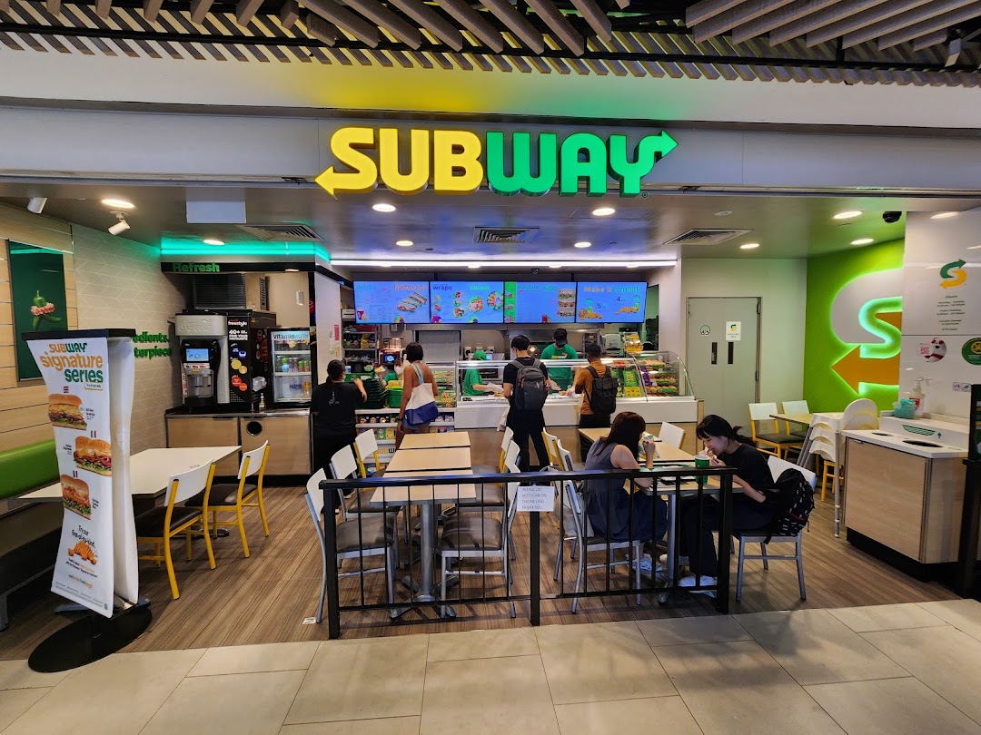 A vibrant Subway restaurant interior with customers, staff, and fresh food displays, showcasing a lively dining atmosphere.