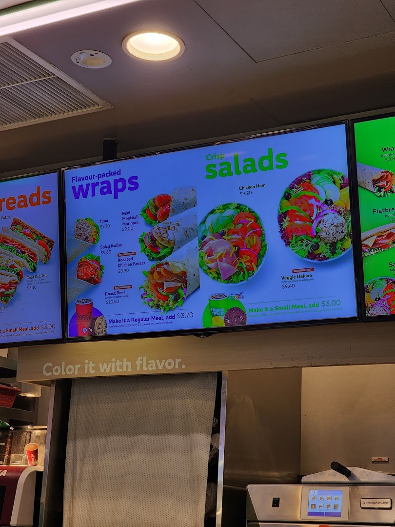 Digital menu boards at Subway displaying wraps, salads, and meal options with prices.