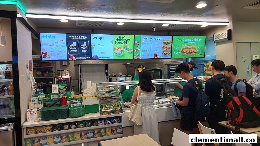 Customers ordering at the counter of a Subway restaurant with digital menu boards displaying various offerings.
