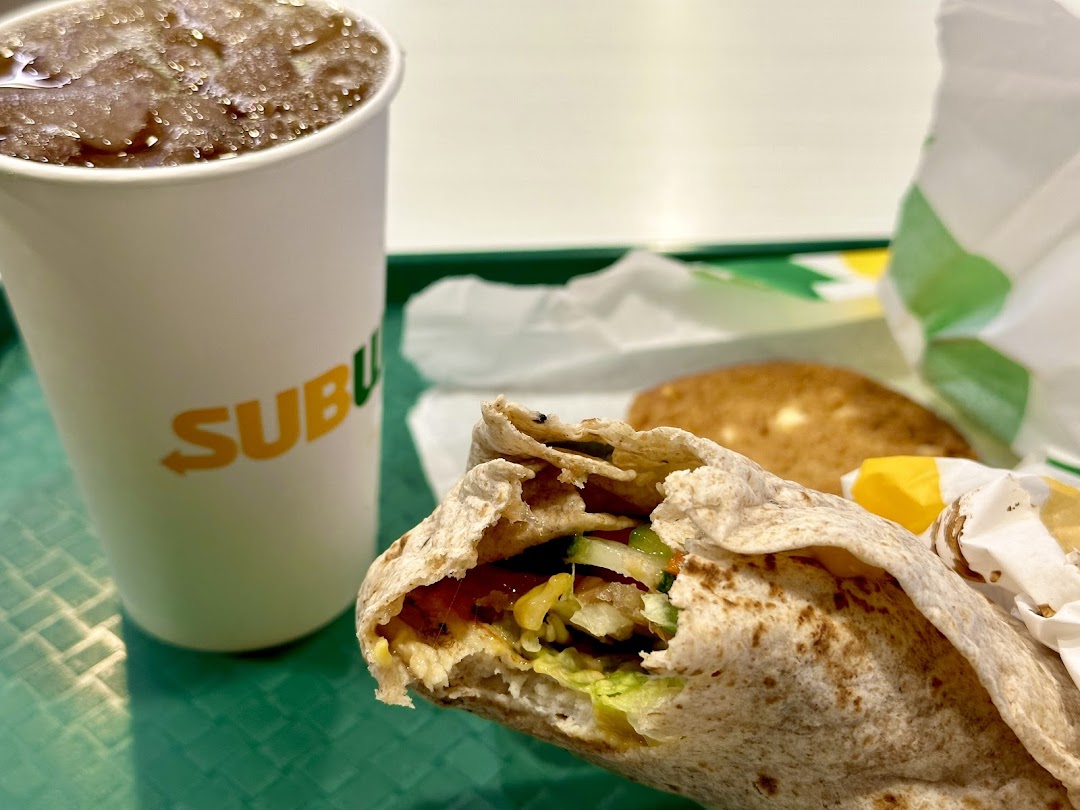 A close-up of a Subway meal featuring a fresh wrap and a refreshing drink on a green tray.