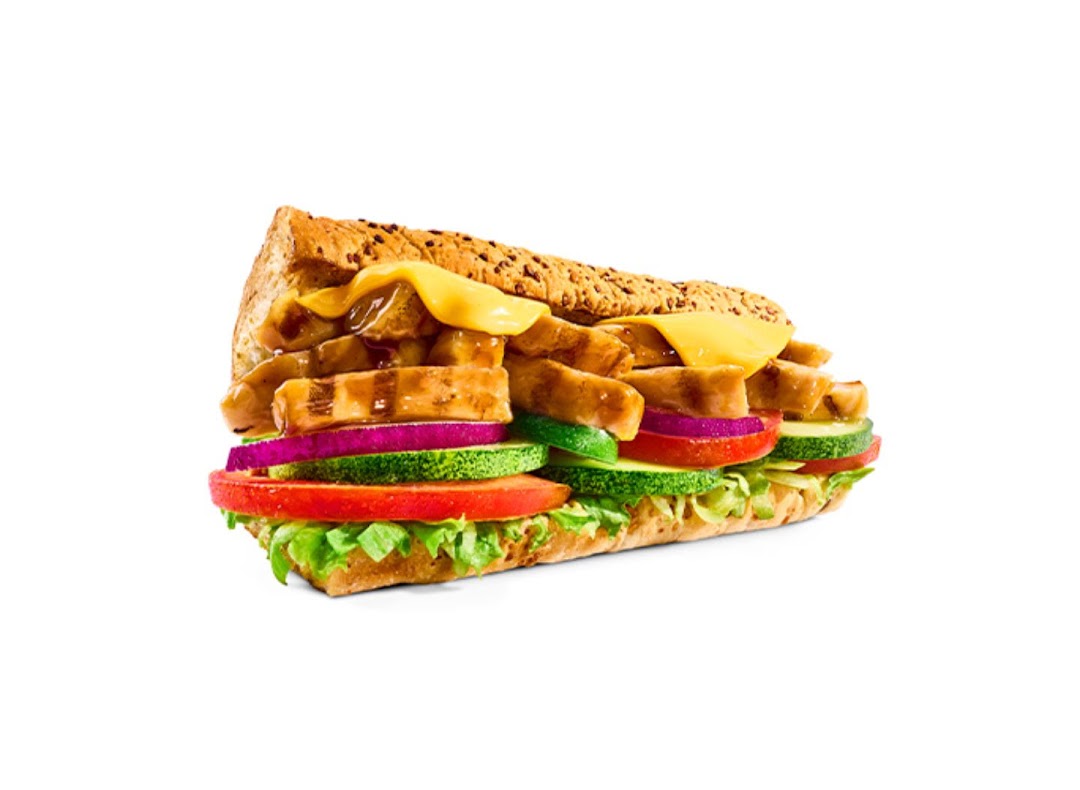 A close-up of a Subway sandwich filled with chicken, melted cheese, and fresh vegetables.