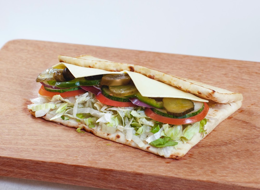A fresh Subway sandwich with various vegetables and cheese on flatbread.