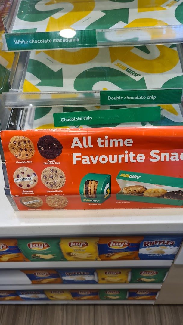 Subway's display case featuring various cookies like chocolate chip and macadamia, alongside popular chip brands.