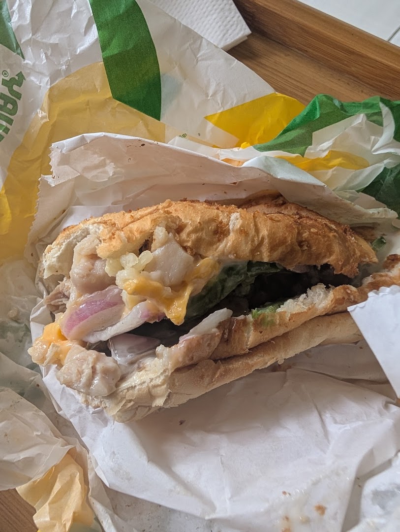 A close-up view of a Subway sandwich, filled with fresh ingredients and partially unwrapped.