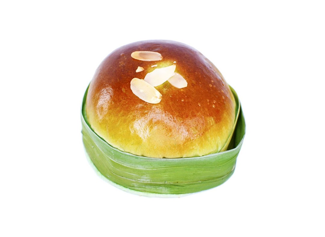 A golden-brown bun topped with almond flakes, served in a green pandan leaf wrapper.
