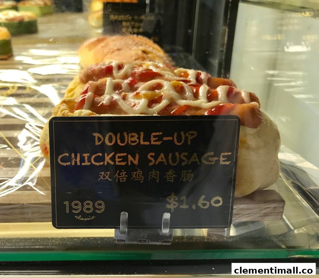 A close-up of a 'Double-Up Chicken Sausage' bun with a price tag in a display case.