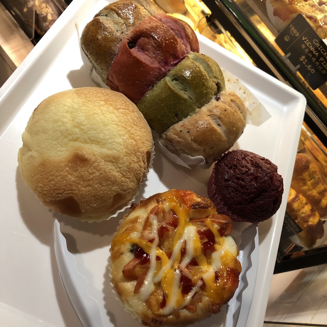 A white tray displays an assortment of freshly baked breads and pastries, including sweet buns and savory pizza bread.