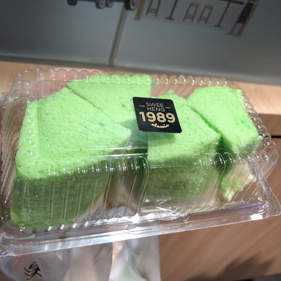 Bright green pandan cake slices in a clear plastic container with a 'Swee Heng 1989 Classic' label.