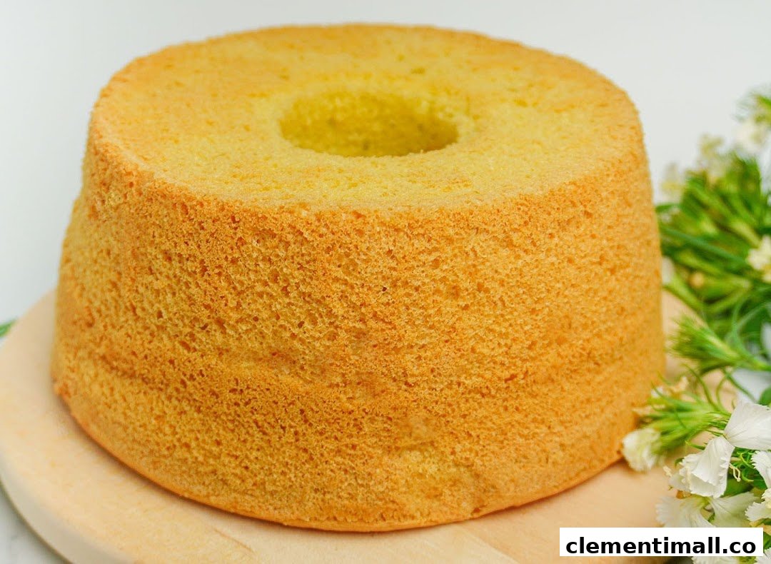 A golden-brown chiffon cake on a wooden board with white flowers.