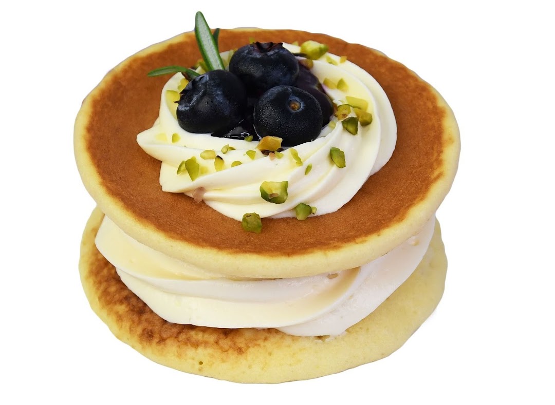 A stack of fluffy pancakes with cream, fresh blueberries, and pistachio sprinkles.