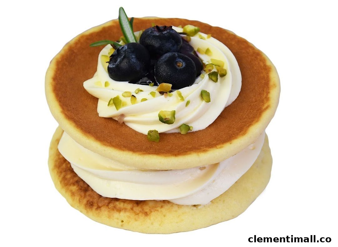 A stack of fluffy pancakes with cream, fresh blueberries, and pistachio sprinkles.