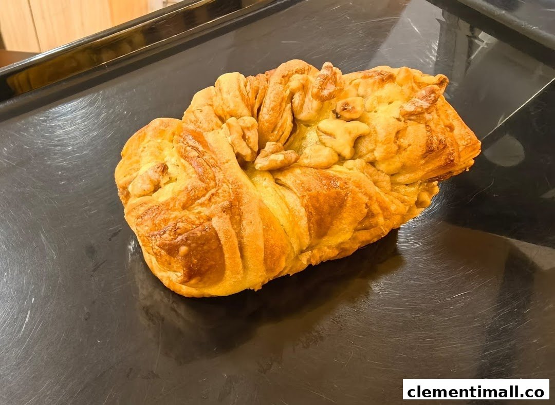 A golden-brown pastry, possibly a bread or bun, topped with walnuts, on a dark baking tray.