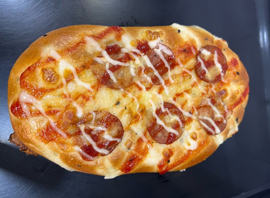 A close-up of a savory bun topped with sausage slices, cheese, and sauces.