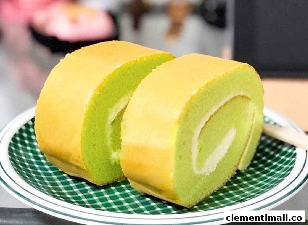 Two slices of vibrant green pandan cake roll with cream filling on a checkered plate.