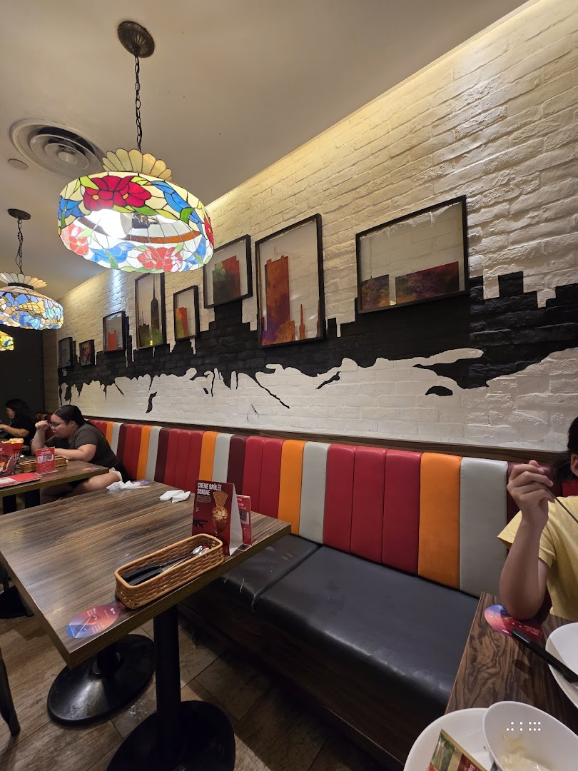 An inviting interior view of Swensen's restaurant, featuring colorful booth seating, wooden tables, and decorative lighting.