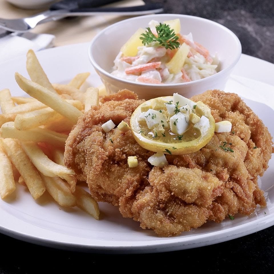 A plate of golden-fried chicken or fish cutlet served with crispy fries, coleslaw, and a lemon garnish.