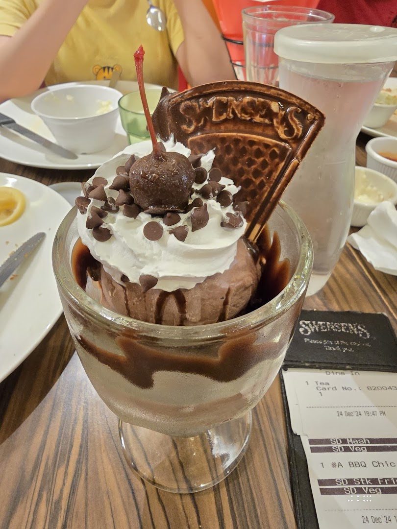A decadent chocolate ice cream sundae with whipped cream, chocolate chips, and a cherry at Swensen's.