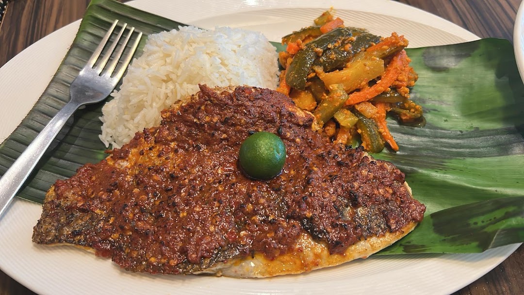 A plate of grilled fish with sambal, white rice, and pickled vegetables, served on a banana leaf.