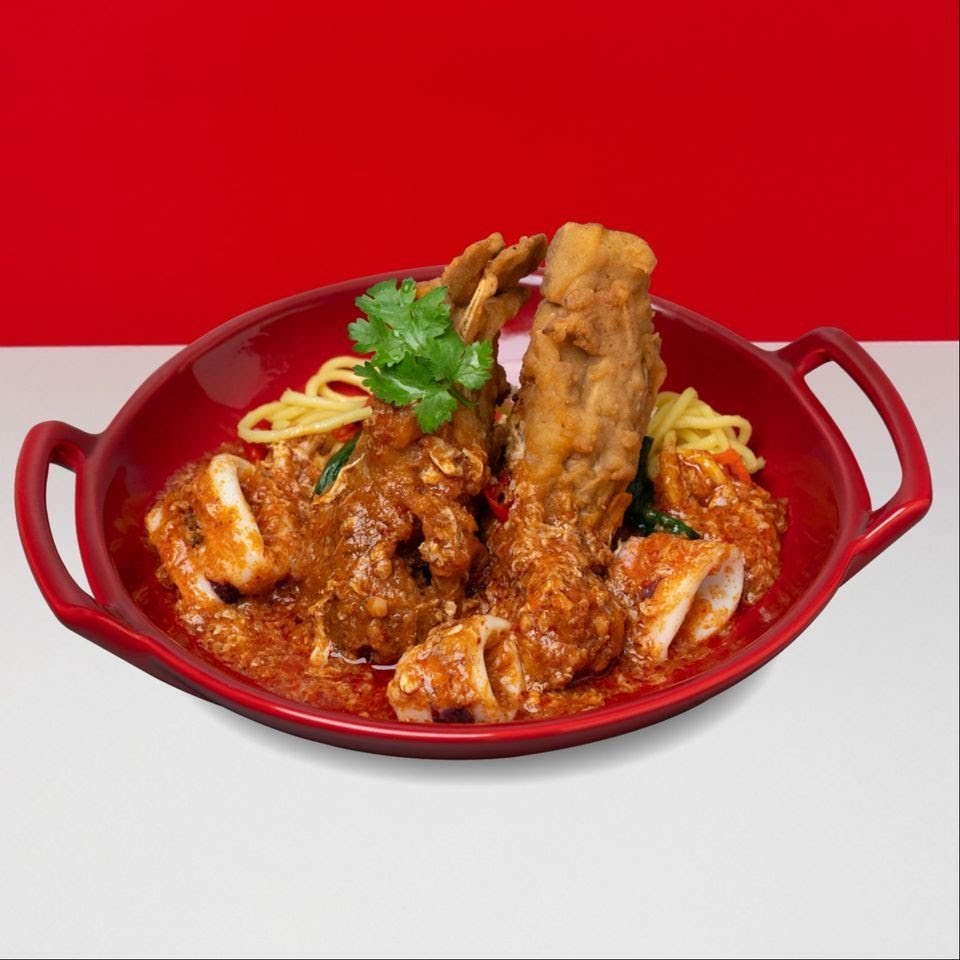 A vibrant red bowl filled with noodles, fried seafood/meat, and squid in a rich, spicy sauce, garnished with cilantro.