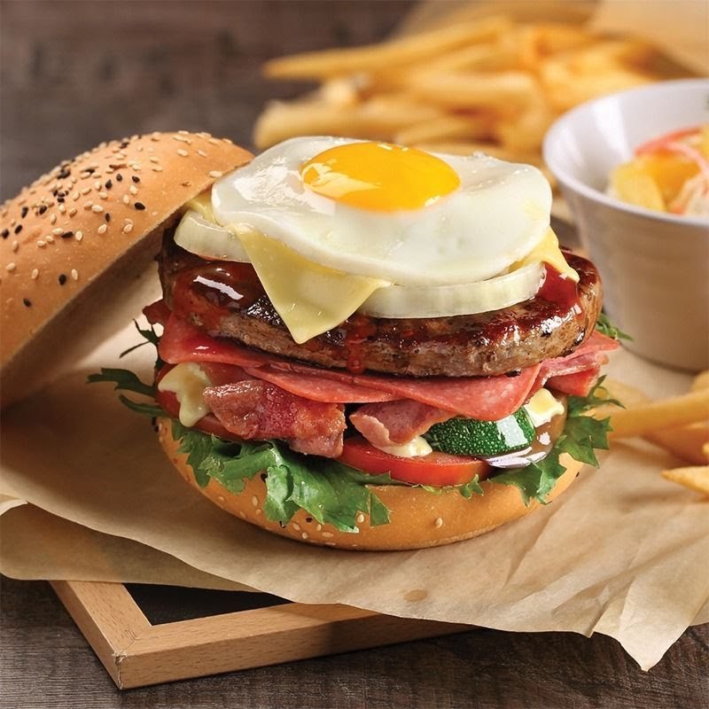 A gourmet burger topped with a fried egg, cheese, and various toppings, served with fries and a fruit salad.