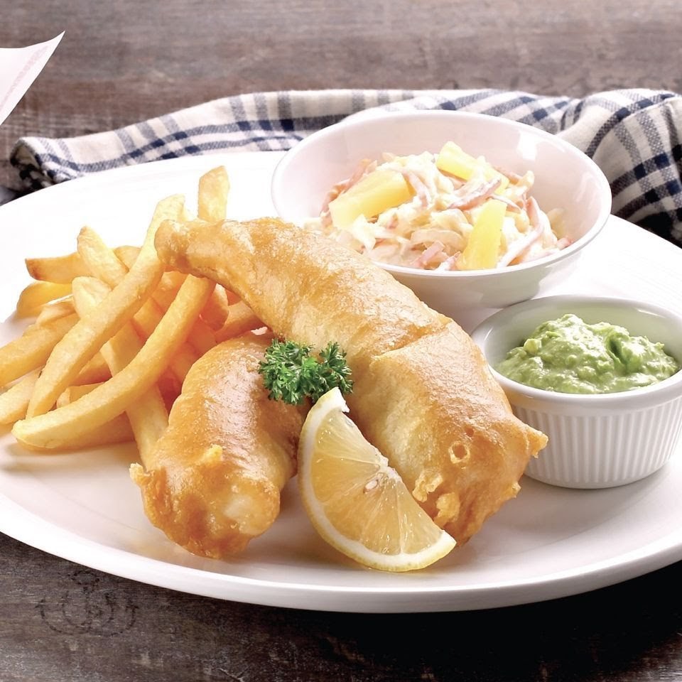 A plate of golden-brown fish and chips served with coleslaw, a lemon wedge, and green dip.