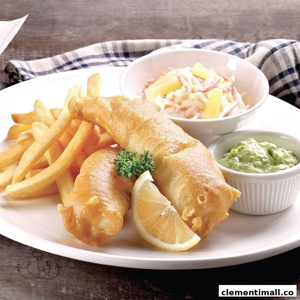 A plate of golden-brown fish and chips served with coleslaw, a lemon wedge, and green dip.