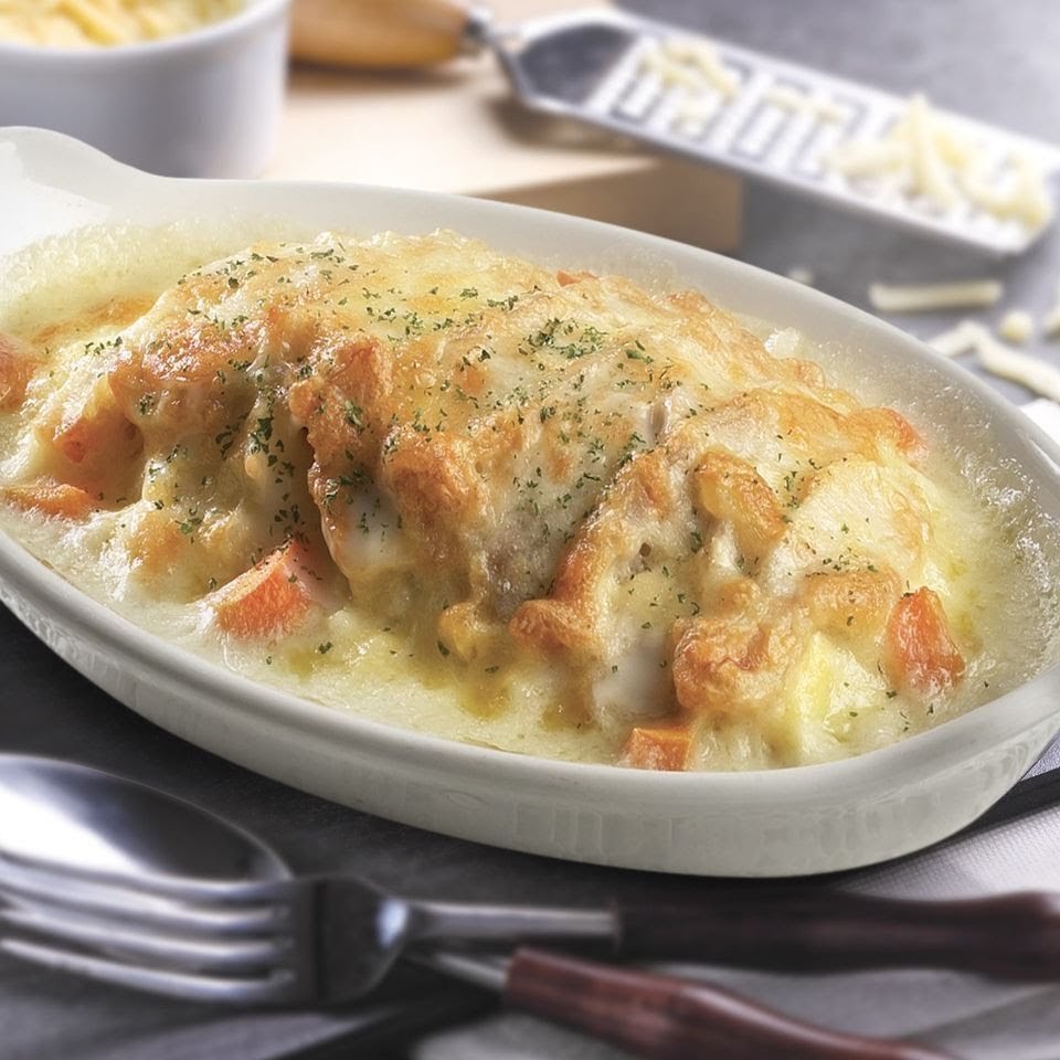 A close-up of a golden-brown baked dish with melted cheese and herbs in a white ceramic dish.