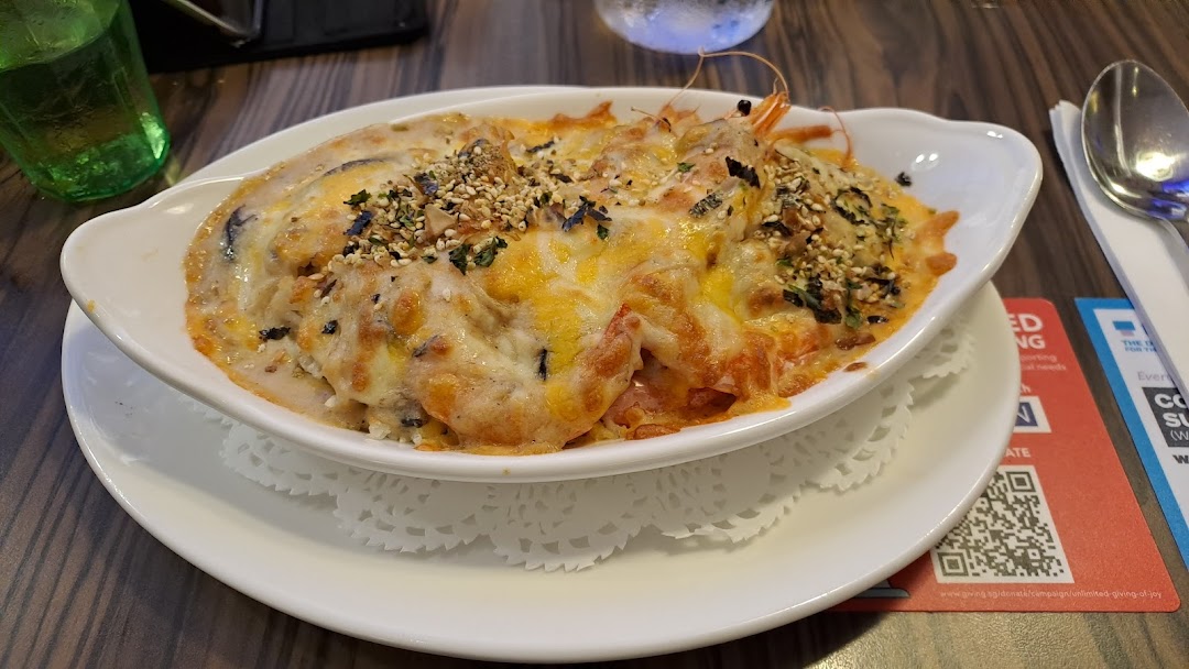 A close-up of a delicious baked cheesy seafood dish, likely with shrimp, served in a white oval bowl.