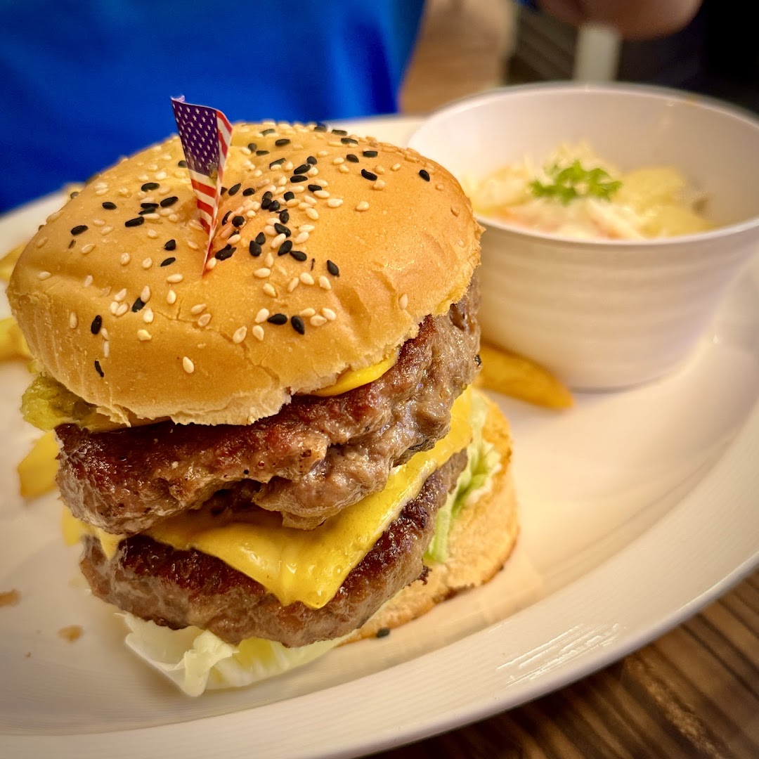 A delicious double-patty cheeseburger with fries and a side dish, served on a white plate.