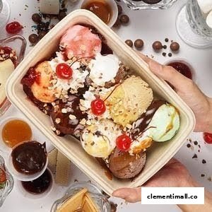 A large takeaway container of colorful ice cream scoops with toppings, held by hands.