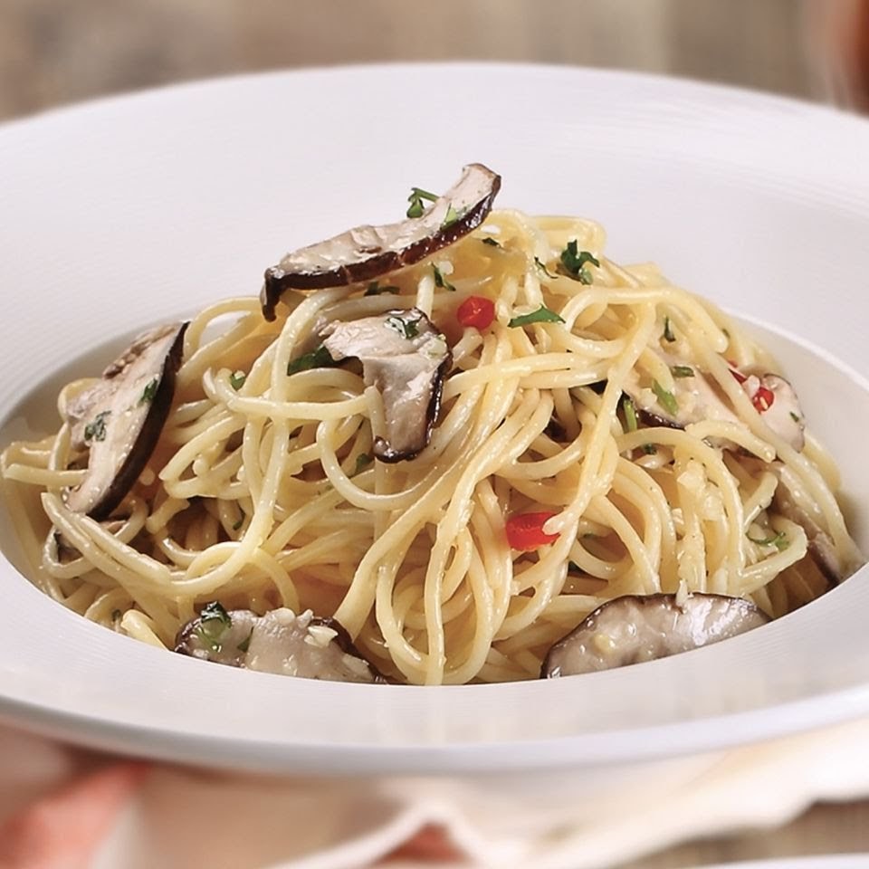 A close-up of a delicious pasta dish with mushrooms, herbs, and chili flakes in a white bowl.