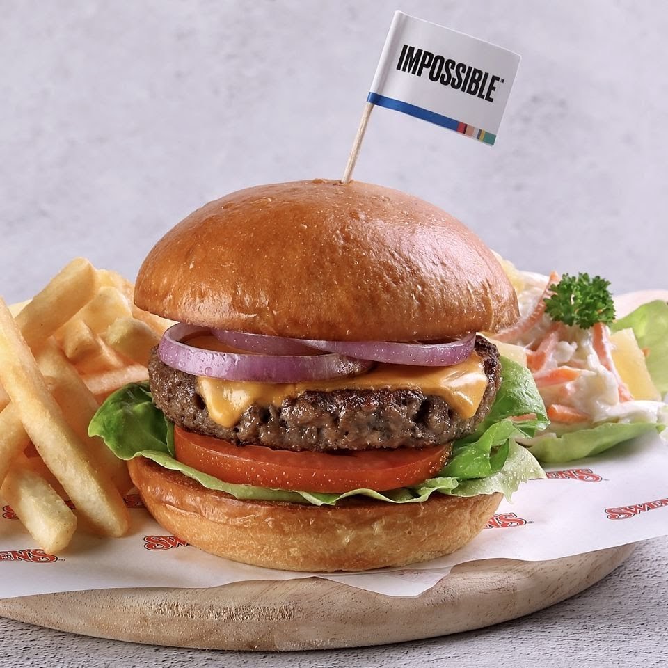 A delicious Impossible burger with cheese, red onions, lettuce, tomato, served with fries and coleslaw.