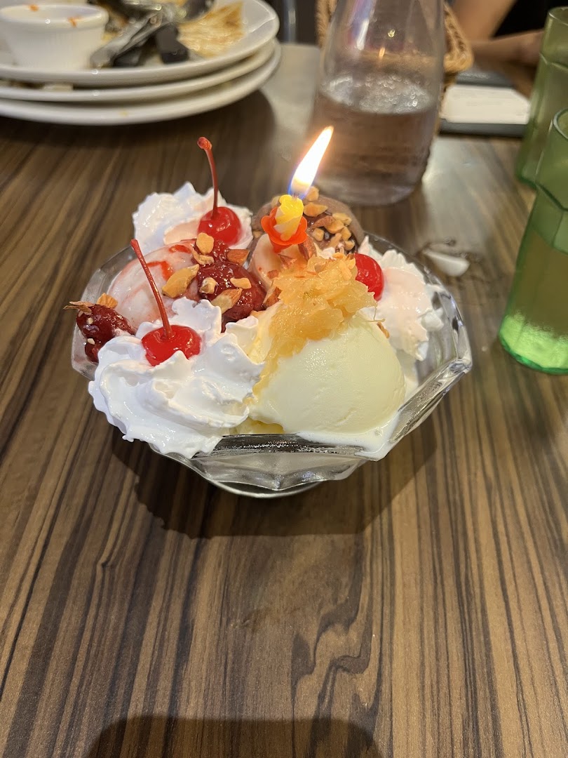 A vibrant ice cream sundae with whipped cream, cherries, and a lit candle, served on a wooden table.