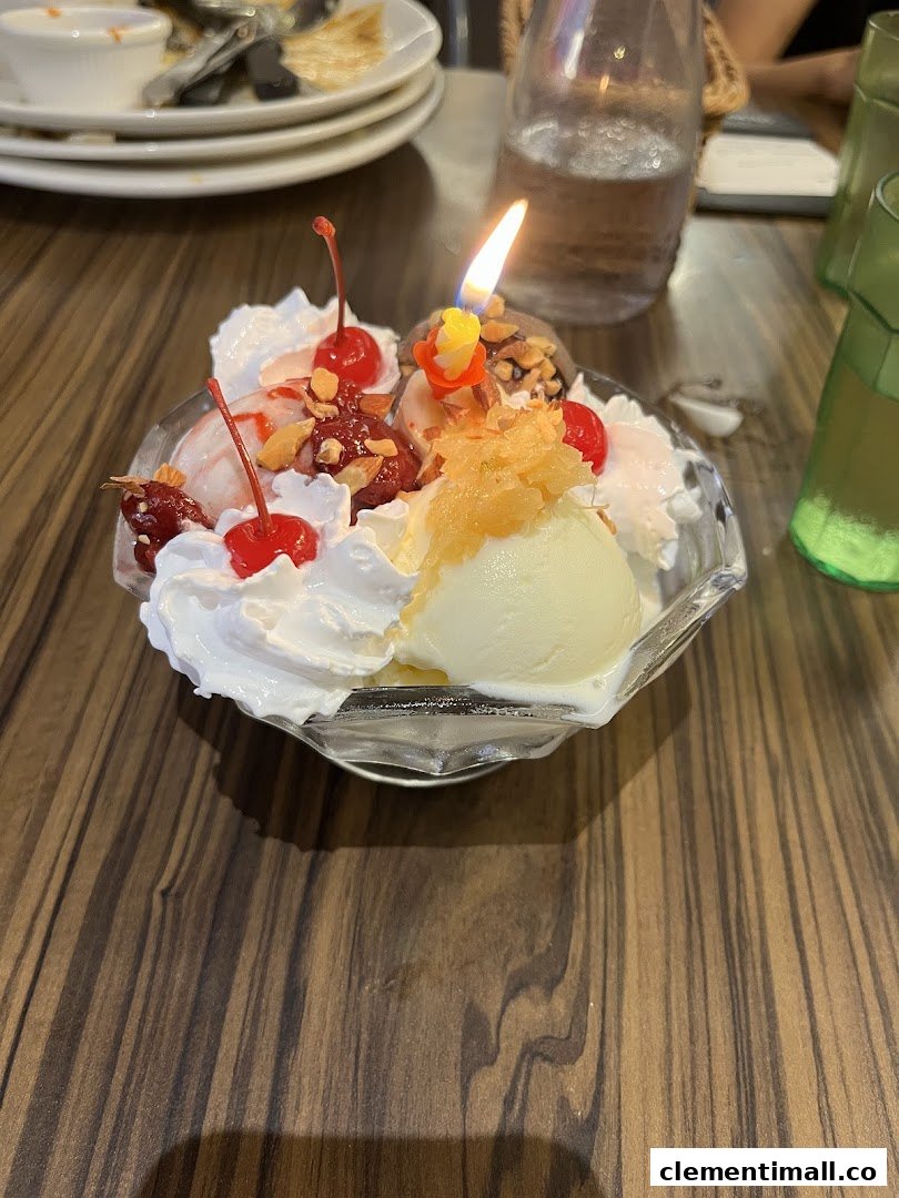 A vibrant ice cream sundae with whipped cream, cherries, and a lit candle, served on a wooden table.