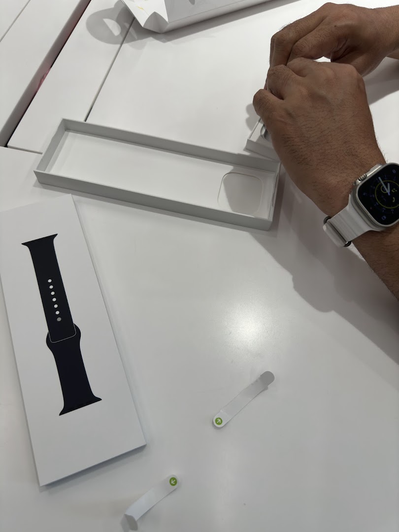 Hands unboxing a new Apple Watch, with packaging and a watch band visible on a white table.