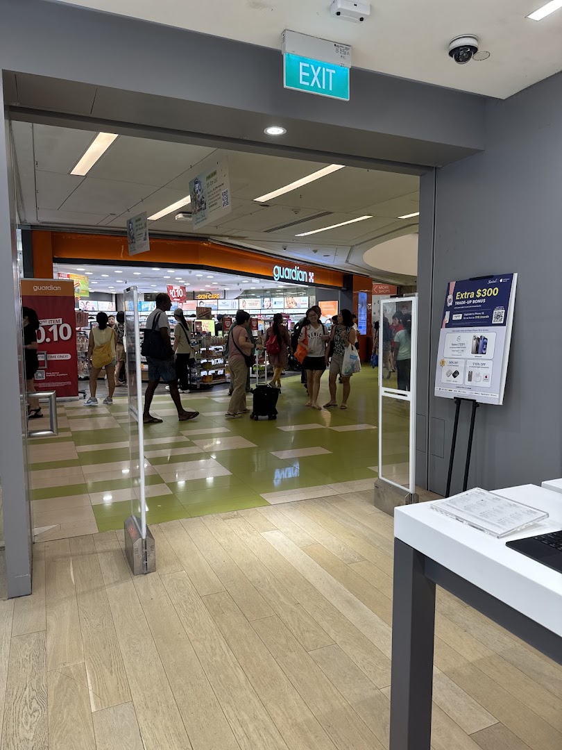 View from a retail store's exit, showing security gates and the mall corridor with shoppers and a Guardian store.