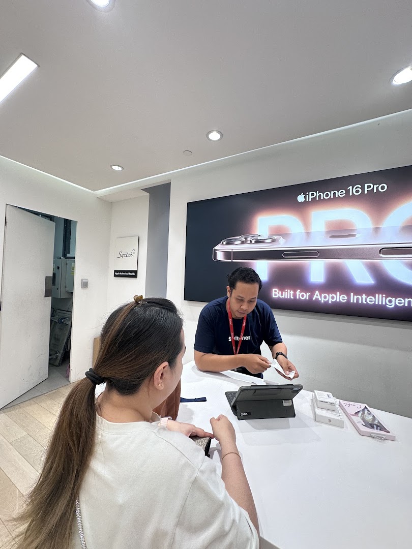 A customer interacts with staff at Switch, an Apple authorized reseller, featuring an iPhone 16 Pro display.