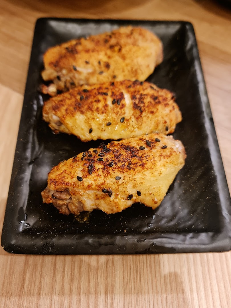 Three golden-brown chicken wings seasoned with black sesame seeds on a black rectangular plate.