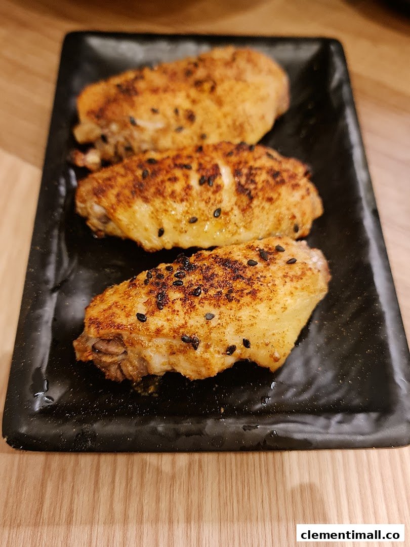 Three golden-brown chicken wings seasoned with black sesame seeds on a black rectangular plate.