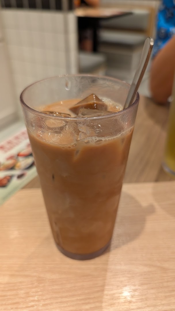 A close-up of a refreshing iced milk tea with ice cubes and a spoon on a wooden table.